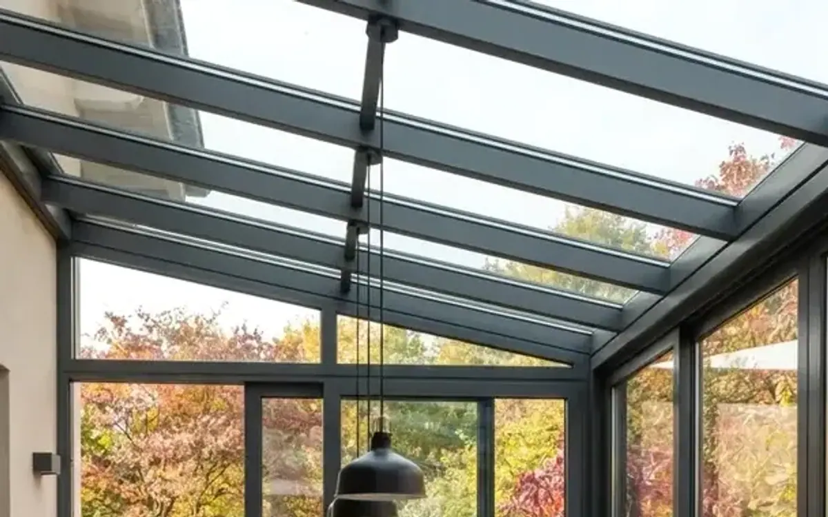 Pendelleuchte unter einem Wintergarten-Glasdach mit Blick in den Herbstgarten
